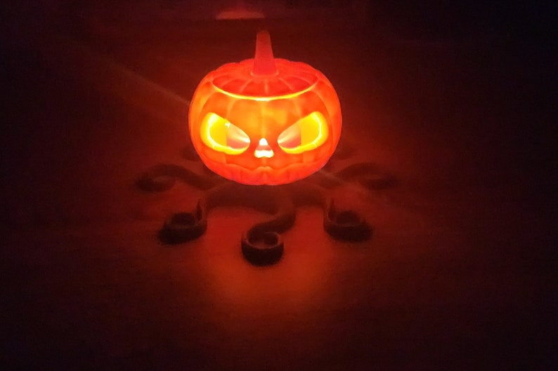 May include: A glowing orange jack-o'-lantern with a scary face sits on a black, octopus-shaped stand.