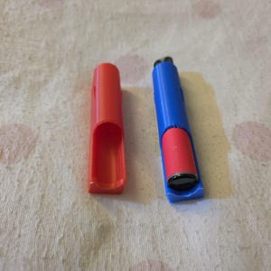 K&ouml;nnte beinhalten: Ein rotes und blaues Feuerzeuggeh&auml;use mit einem Feuerzeug darin. Das Geh&auml;use besteht aus Kunststoff und hat eine rechteckige Form. Das Feuerzeug ist rot und schwarz. Das Geh&auml;use ist offen und das Feuerzeug ist sichtbar.