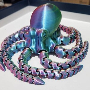May include: A 3D printed iridescent octopus with eight tentacles. The octopus is a vibrant blue, green, and pink colour.