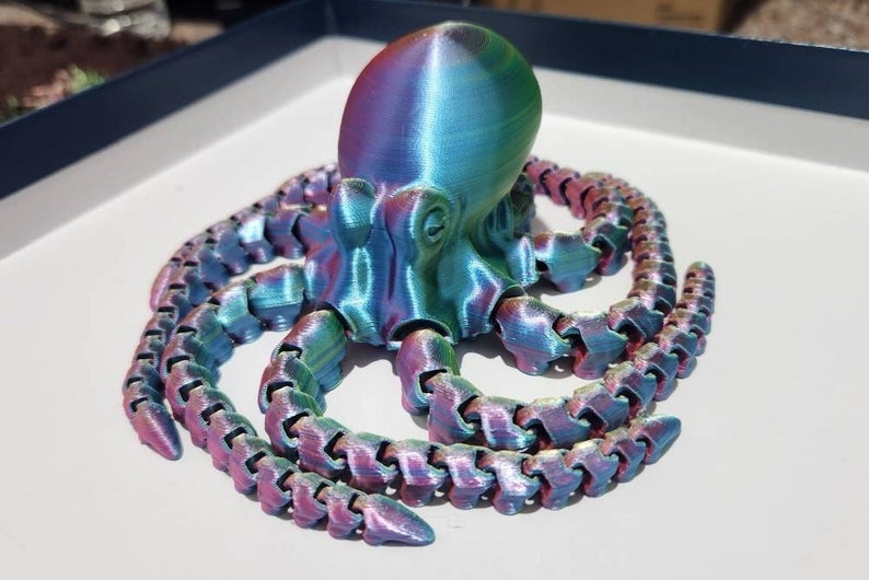 May include: A 3D printed iridescent octopus with eight tentacles. The octopus is a vibrant blue, green, and pink colour.