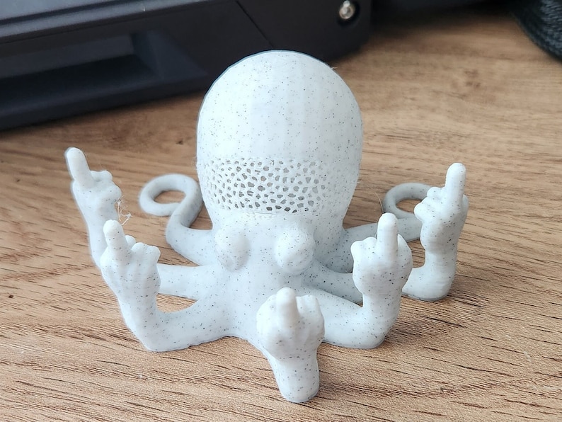 May include: A white, speckled, 3D printed octopus figurine with all eight tentacles raised in a middle finger gesture.