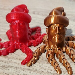 Puede incluir: Dos figuritas de pulpo impresas en 3D con cabezas humanas que llevan gorros de Pap&aacute; Noel. Un pulpo es rojo y el otro es cobre.