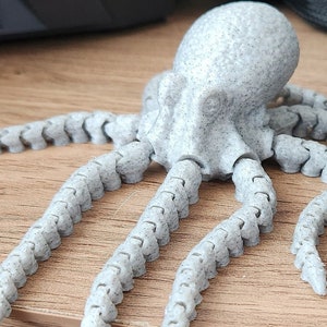 May include: A grey, articulated octopus figurine with a textured surface. The octopus has eight flexible tentacles.
