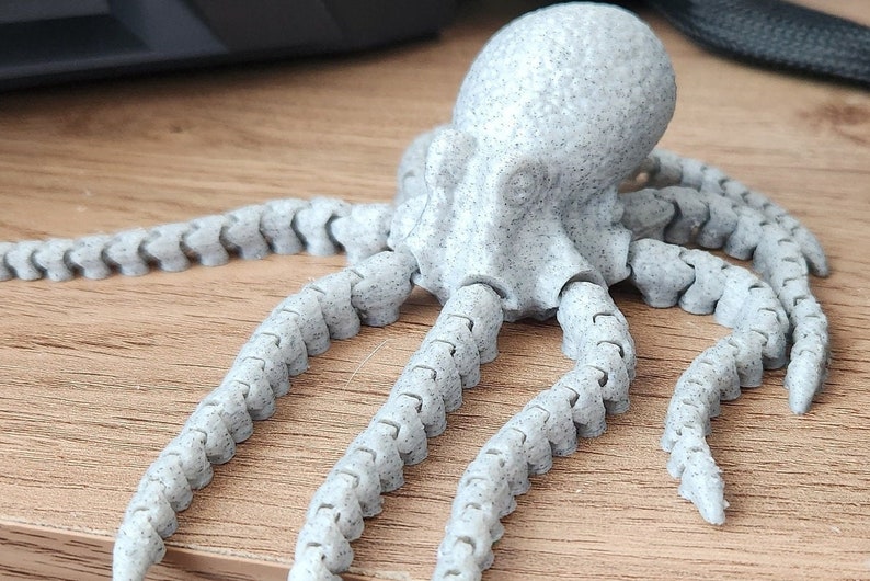 May include: A grey, articulated octopus figurine with a textured surface. The octopus has eight flexible tentacles.