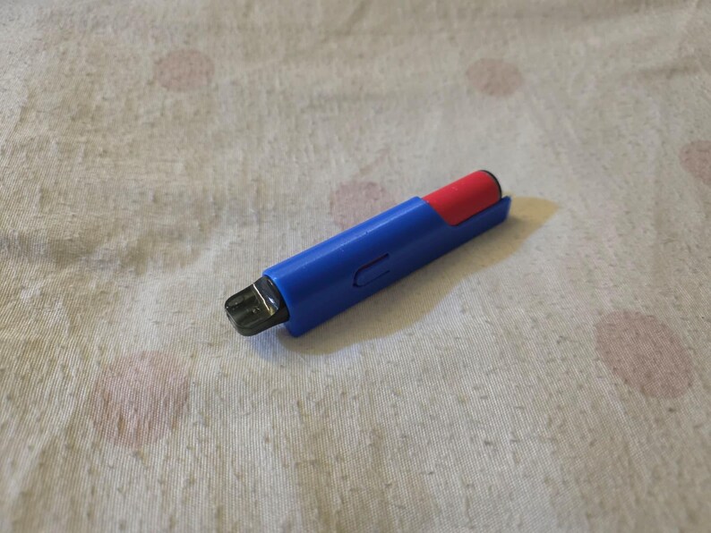 K&ouml;nnte beinhalten: Ein blau-roter Vape-Pen mit schwarzem Mundst&uuml;ck. Der Stift liegt auf einer wei&szlig;-beigen Oberfl&auml;che mit Muster. Der Vape-Pen hat eine rechteckige Form mit abgerundeten Kanten.