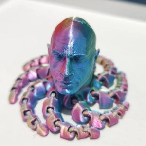 Op de afbeelding: Een 3D-geprint hoofdbeeld met een iriserende blauwe, roze en paarse afwerking. Het hoofd is omringd door een ketting van met elkaar verbonden 3D-geprinte stukken.