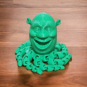 Puede incluir: Una figura impresa en 3D de color verde de la cabeza de Shrek con una expresi&oacute;n sonriente, unida a un cuerpo verde de pulpo con m&uacute;ltiples tent&aacute;culos.