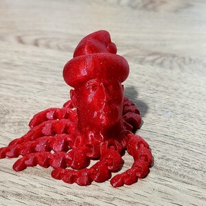 Puede incluir: Una figura roja impresa en 3D de una persona con un sombrero y un cuerpo de pulpo rojo.