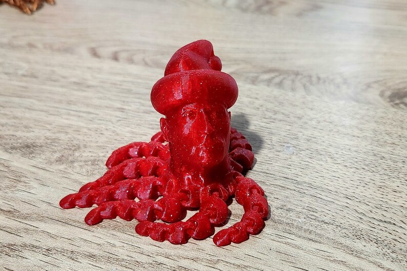 Puede incluir: Una figura roja impresa en 3D de una persona con un sombrero y un cuerpo de pulpo rojo.