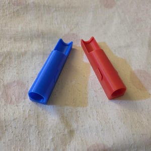 K&ouml;nnte beinhalten: Zwei Plastikpfeifen, eine blaue und eine rote, liegen diagonal auf einer strukturierten, cremefarbenen Oberfl&auml;che. Die Pfeifen haben einen zylindrischen K&ouml;rper mit einem gebogenen Mundst&uuml;ck. Die blaue Pfeife ist links, die rote rechts.