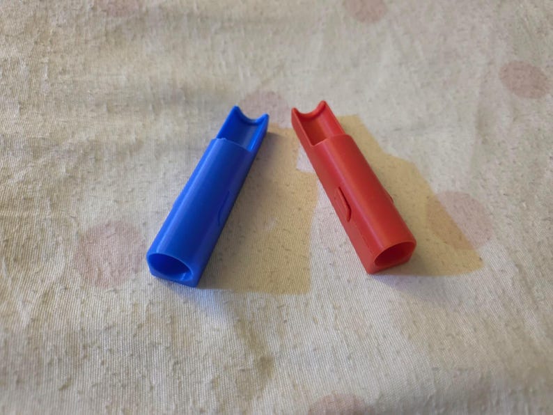 K&ouml;nnte beinhalten: Zwei Plastikpfeifen, eine blaue und eine rote, liegen diagonal auf einer strukturierten, cremefarbenen Oberfl&auml;che. Die Pfeifen haben einen zylindrischen K&ouml;rper mit einem gebogenen Mundst&uuml;ck. Die blaue Pfeife ist links, die rote rechts.
