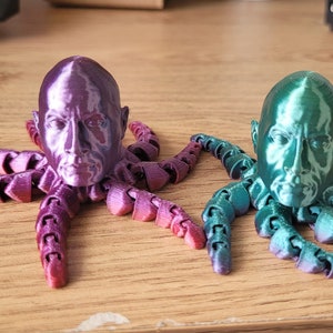 Op de afbeelding: Twee 3D-geprinte octopus-beeldjes met menselijke gezichten. De octopus links is paars en de octopus rechts is groen.