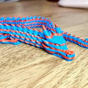 Puede incluir: Una figurita de drag&oacute;n de pl&aacute;stico azul y rojo con un cuerpo segmentado. El drag&oacute;n tiene una cola larga y una cabeza detallada con dientes afilados.