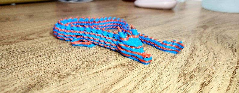 Puede incluir: Una figurita de drag&oacute;n de pl&aacute;stico azul y rojo con un cuerpo segmentado. El drag&oacute;n tiene una cola larga y una cabeza detallada con dientes afilados.