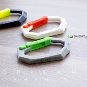 May include: Three 3D printed origami carabiners in black, white, and gray with green, red, and yellow accents. The carabiners are labeled "ENERDESIGN" and "ddf3d.com".