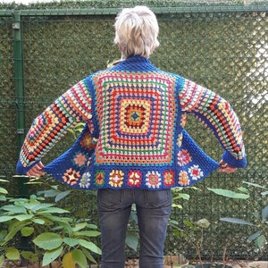 May include: A blue crochet cardigan with a colourful granny square pattern. The cardigan is open at the front and has long sleeves.
