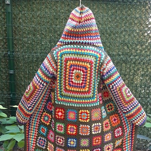 May include: A vibrant, hand-crocheted coat with a hood. The coat showcases a patchwork design with numerous square patterns in red, orange, yellow, green, blue, and purple. The coat is long and covers the legs.