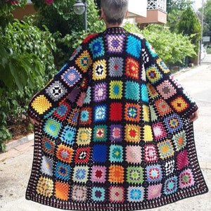 Puede incluir: Una chaqueta de ganchillo colorida con un patrón de cuadrados de la abuela. La chaqueta es negra con cuadrados de varios colores, incluyendo rojo, azul, verde, amarillo y rosa.