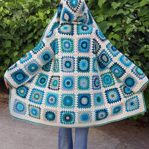 May include: A crocheted cardigan with a hood, featuring a patchwork design of granny squares in shades of blue, green, and white.
