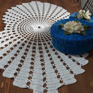 Pode incluir: Um corredor de mesa de crochê branco com um design circular. O corredor está sobre uma mesa de madeira com duas caixas azuis e brancas com flores brancas no topo.