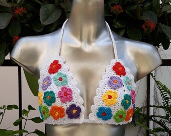Op de afbeelding: Een wit gehaakt bikini-topje met kleurrijke bloemenaccenten. Het topje is gemaakt van wit gehaakt stof en heeft een verscheidenheid aan kleurrijke bloemen.