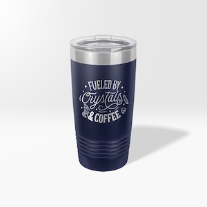 May include: A navy blue stainless steel tumbler with a white design that says "Fueled by Crystals & Coffee".