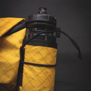 May include: A yellow water bottle holder with a black water bottle inside. The holder has a black strap and a diamond pattern.