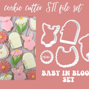 Może przedstawiać: Zestaw foremek do ciasteczek w kształcie baby. Formy do ciasteczek obejmują body dla dziecka, kwiat, śliniak, baner z tekstem "Baby in Bloom" i mały okrągły wycinak. Formy do ciasteczek są białe i pokazane na różowym tle.