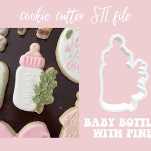 May include: A white cookie cutter shaped like a baby bottle with a pine branch on the side. The text "BABY BOTTLE WITH PINE" is written below the cutter.