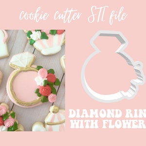 Pode incluir: Cortador de biscoitos de plástico branco em forma de anel de diamante com flores. O anel tem uma forma de diamante na parte superior e uma banda com um design floral no lado. O cortador está sobre um fundo rosa com o texto "DIAMOND RING WITH FLOWERS" abaixo.