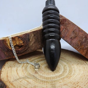 May include: A black wooden pendulum with a silver chain. The pendulum is resting on a wooden surface.