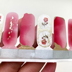 Peut inclure: Bandes de nail art avec un effet aquarelle rose et blanc, orn&eacute;es de feuilles d'or et de motifs de roses. Les d&eacute;calcomanies &agrave; ongles sont pr&eacute;sent&eacute;es sur un support argent&eacute;.