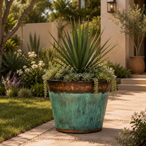 May include: A large, tapered metal planter featuring a weathered, oxidised finish with a vibrant turquoise-green patina on the lower section and a dark, rustic bronze-toned rim, containing a spiky green agave plant and trailing succulents.