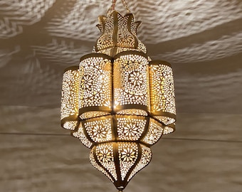 Puede incluir: Lámpara colgante dorada y ornamentada con intrincados patrones calados. La luz proyecta sombras decorativas en el techo. La lámpara tiene un diseño detallado de varios niveles, con una base puntiaguda y una parte superior decorativa.