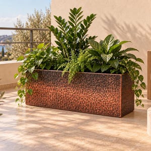 May include: A rectangular planter with a hammered copper finish containing a variety of green houseplants, including a tall Zamioculcas zamiifolia, a fern, and trailing pothos vines, creating a dense arrangement of foliage within the container.