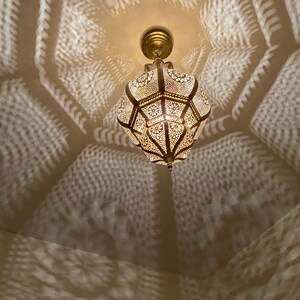 May include: Ornate, gold-colored pendant light with intricate cut-out patterns, casting decorative shadows on the ceiling. The light fixture is suspended from a matching gold ceiling mount, creating a warm, inviting ambiance.
