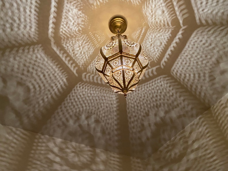 May include: Ornate, gold-colored pendant light with intricate cut-out patterns, casting decorative shadows on the ceiling. The light fixture is suspended from a matching gold ceiling mount, creating a warm, inviting ambiance.
