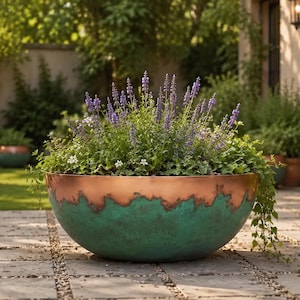 Puede incluir: Una maceta grande en forma de cuenco con un borde superior de cobre metálico y una base texturizada de color verde azulado estilo verdigris. La maceta está llena de follaje verde variado y espigas de flores moradas altas y delgadas.
