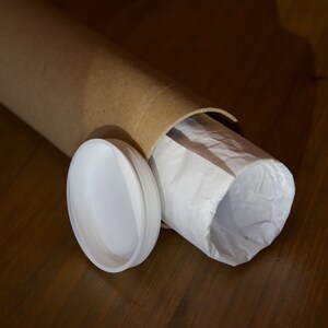 Puede incluir: Un tubo de cart&oacute;n marr&oacute;n con un forro de papel blanco en el interior. El tubo est&aacute; parcialmente desenrollado, revelando el forro de papel blanco. Una tapa de pl&aacute;stico blanco est&aacute; situada junto al tubo.
