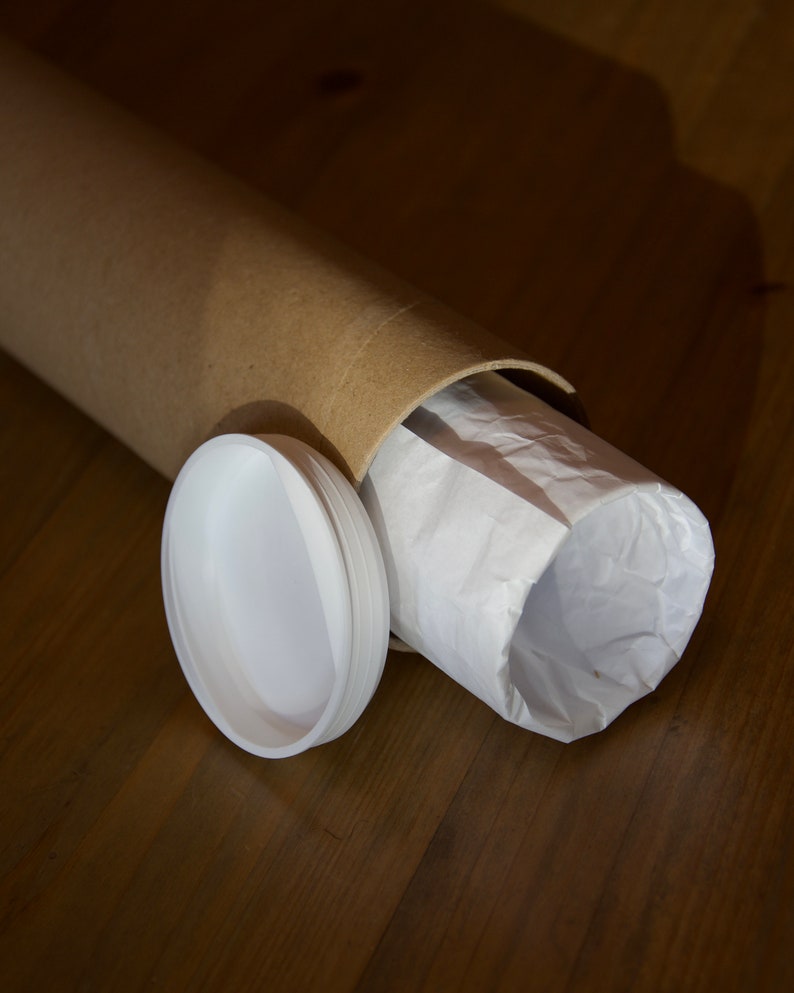 Puede incluir: Un tubo de cart&oacute;n marr&oacute;n con un forro de papel blanco en el interior. El tubo est&aacute; parcialmente desenrollado, revelando el forro de papel blanco. Una tapa de pl&aacute;stico blanco est&aacute; situada junto al tubo.
