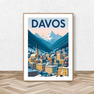 May include: A framed art print featuring the word "DAVOS" in navy blue above a stylized illustration of a snow-covered town nestled in a valley. The artwork depicts buildings, a church steeple, and snow-capped mountains.