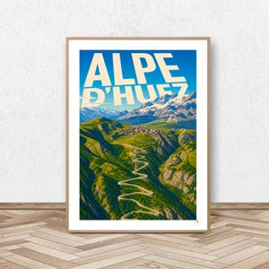 Peut inclure: Une affiche de voyage encadrée représentant une route sinueuse menant au village de montagne de l'Alpe d'Huez. L'illustration montre des pentes vertes, des falaises rocheuses et des sommets enneigés sous un ciel bleu avec le texte ALPE D'HUEZ.