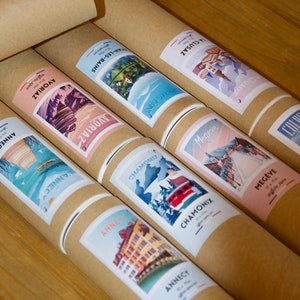 Puede incluir: Una colecci&oacute;n de tubos de cart&oacute;n marr&oacute;n con etiquetas coloridas que muestran ilustraciones de varias ciudades y pueblos franceses. Las etiquetas incluyen los nombres de las ciudades y pueblos, como Annecy, Chamonix y Meg&egrave;ve.
