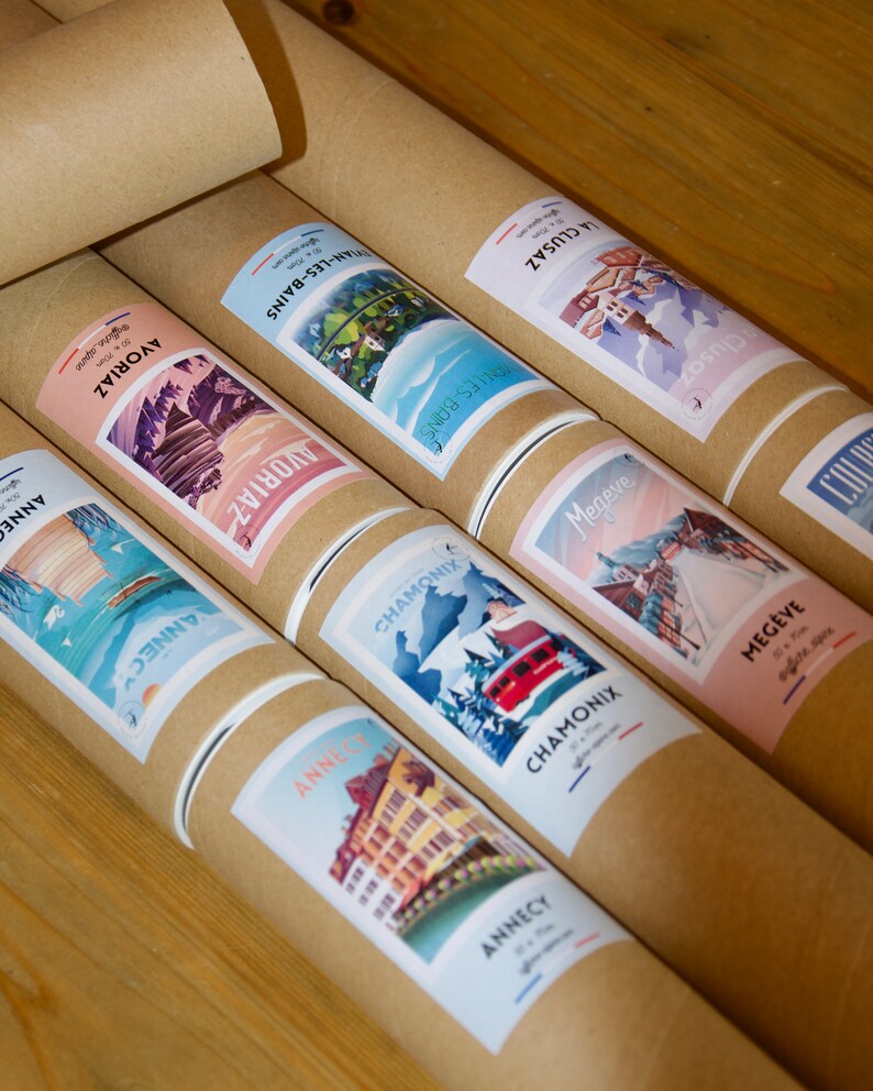 Puede incluir: Una colecci&oacute;n de tubos de cart&oacute;n marr&oacute;n con etiquetas coloridas que muestran ilustraciones de varias ciudades y pueblos franceses. Las etiquetas incluyen los nombres de las ciudades y pueblos, como Annecy, Chamonix y Meg&egrave;ve.