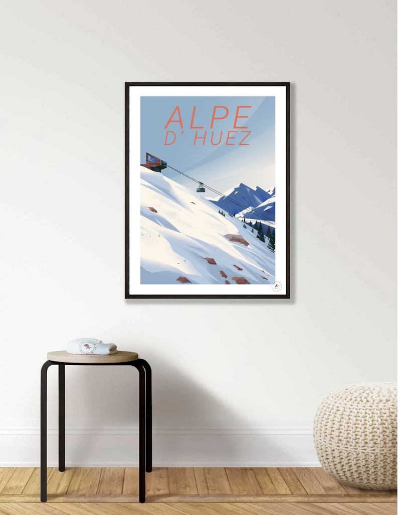 Puede incluir: Un p&oacute;ster enmarcado en negro con una ilustraci&oacute;n azul y blanca de un telesilla subiendo una monta&ntilde;a nevada. El texto "ALPE D'HUEZ" est&aacute; en letras rojas en la parte superior del p&oacute;ster.