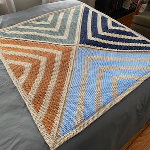 May include: A crocheted blanket with a geometric pattern in shades of blue, orange, and beige.
