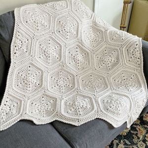 May include: A white crocheted blanket with a hexagonal pattern. The blanket is draped over a gray couch.