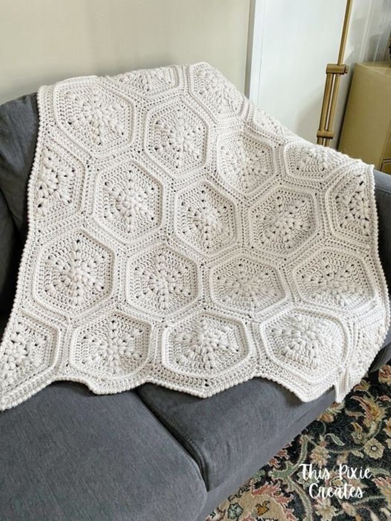 May include: A white crocheted blanket with a hexagonal pattern. The blanket is draped over a gray couch.