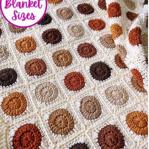 K&ouml;nnte beinhalten: Eine geh&auml;kelte Decke mit einem sich wiederholenden Muster aus braunen, beigen und orangen Kreisen auf wei&szlig;em Hintergrund. Die Decke ist zur H&auml;lfte gefaltet und der Text "9 Blanket Sizes" ist in der oberen linken Ecke sichtbar.
