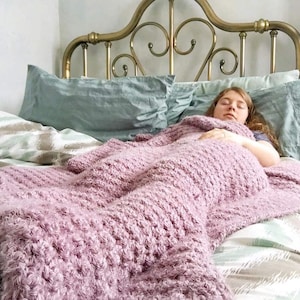 May include: A person sleeping under a soft, pink, fuzzy blanket on a bed with a brass headboard.